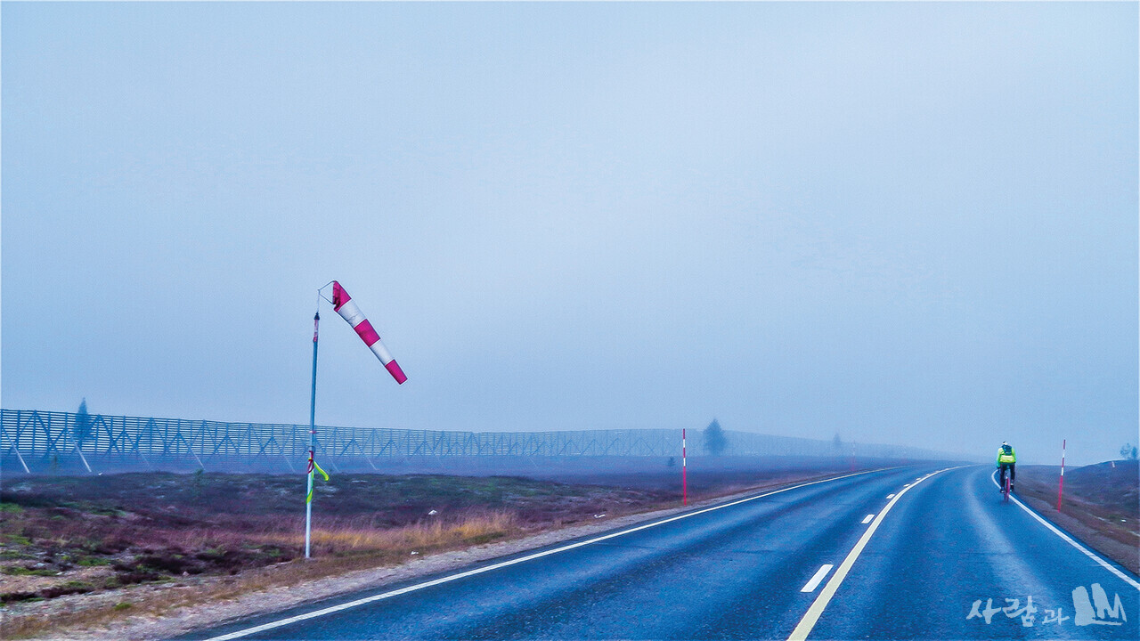 안개비를 맞고 스웨덴과 국경으로 보이는 철책을 따라 가고 있는 자전거 순례자.